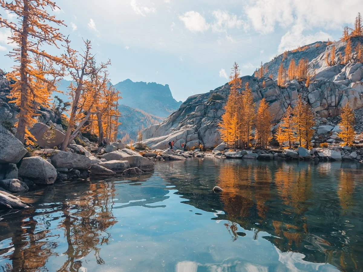 tiny hikers, hiking around a lake in the core enchantments with golden larch trees surrounding them