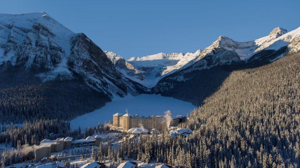 looking down at the fairmont hotel in lake louise, along with a frozen lake louise and snowy mountains in the background
