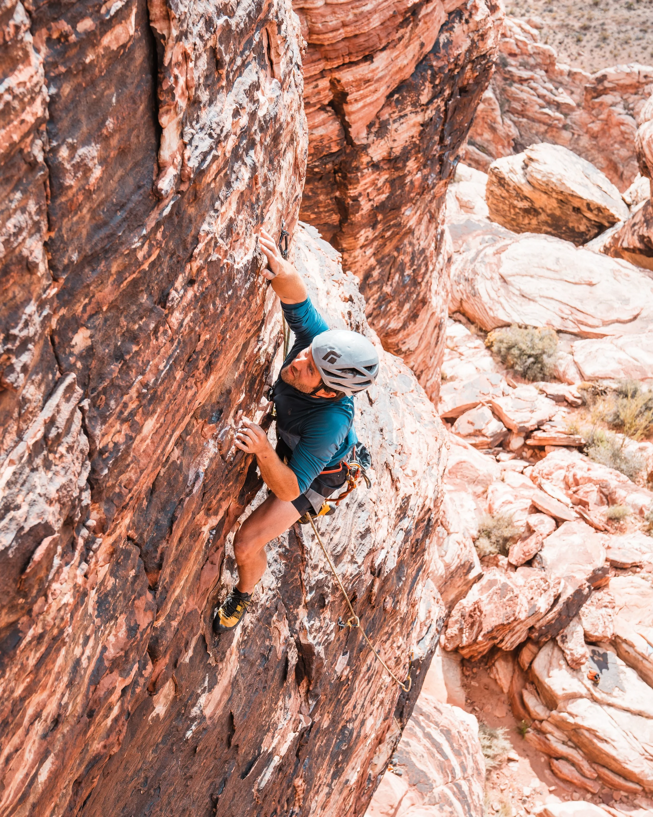 A man rock climbing on a red sandstone cliff, wearing a helmet and climbing gear, in a desert landscape.