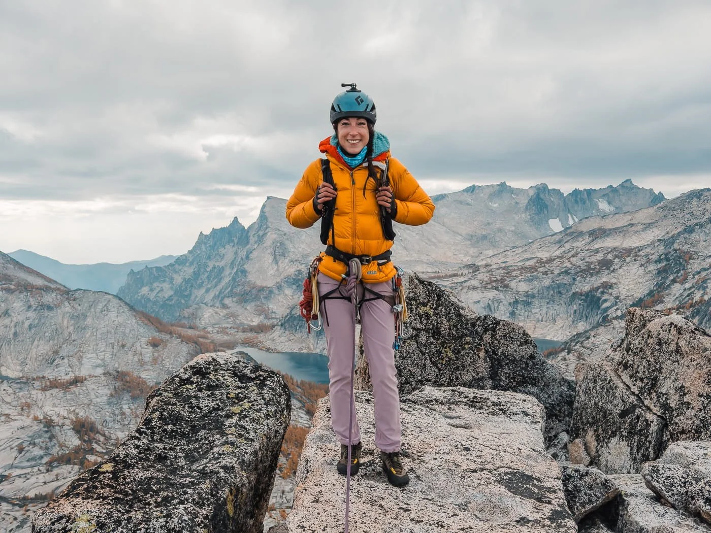 a climber standing on the summit of prusik peak in the enchantments, wearing a puffy down jacket and a lot of layers