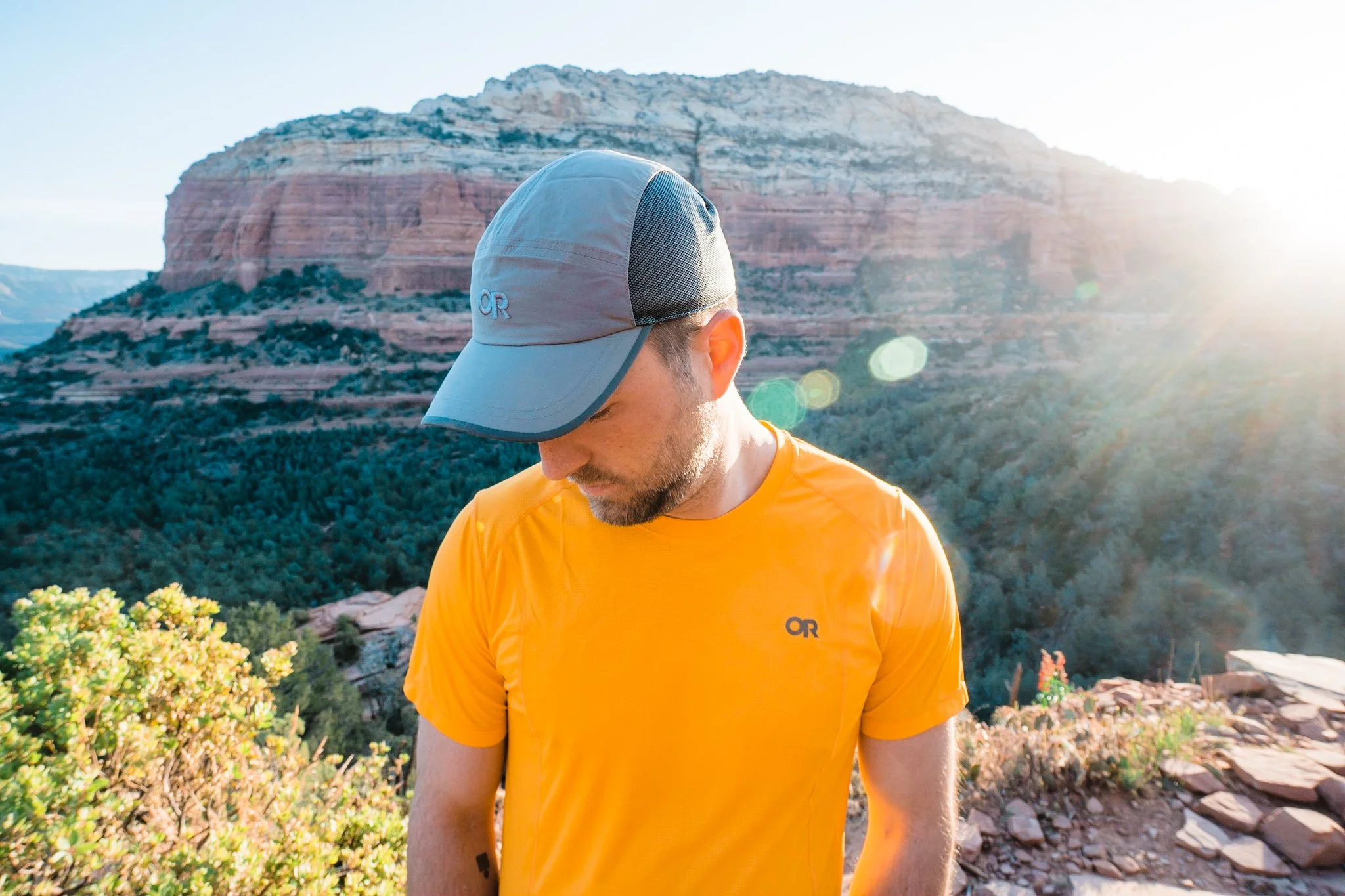 a man wearing a grey cap and yellow sun shirt standing in front of red rocks in sedona