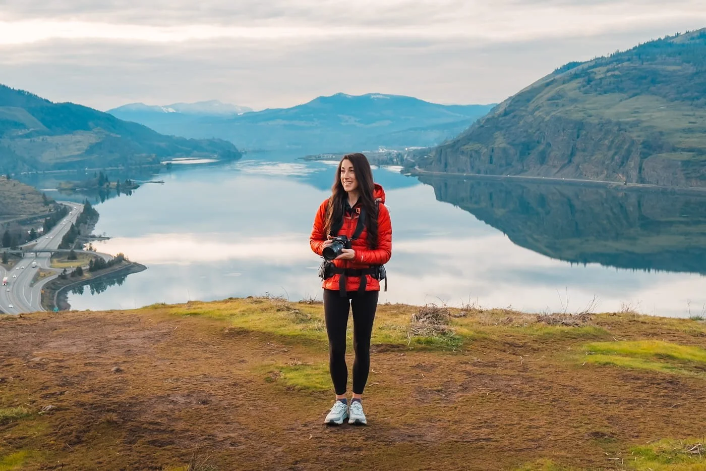 a woman at an overlook of the Columbia River Gorge in Oregon, wearing a red jacket and holding her camera