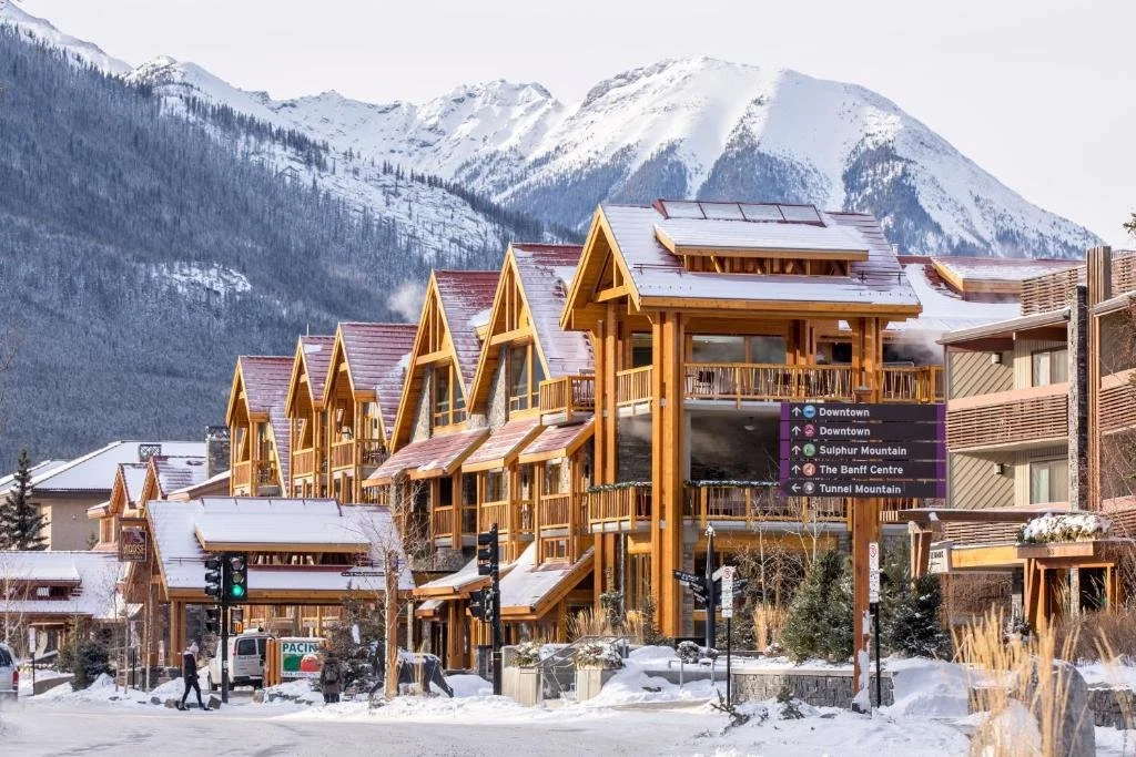 a hotel in downtown banff covered in snow, with mountains in the background