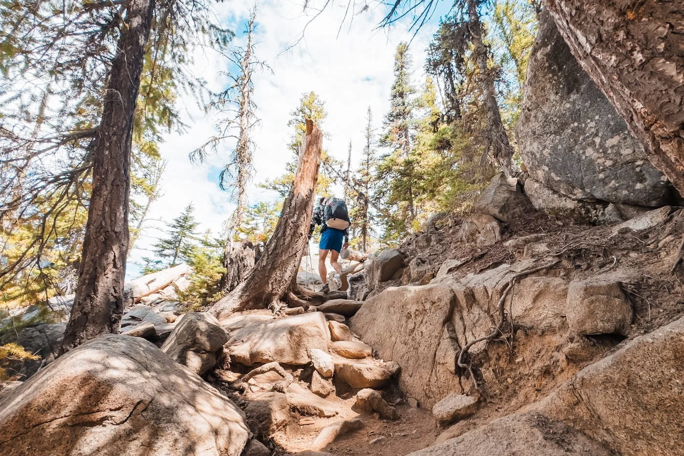 a backpacker hiking up a rocky trail, through a forest to colchuck lake