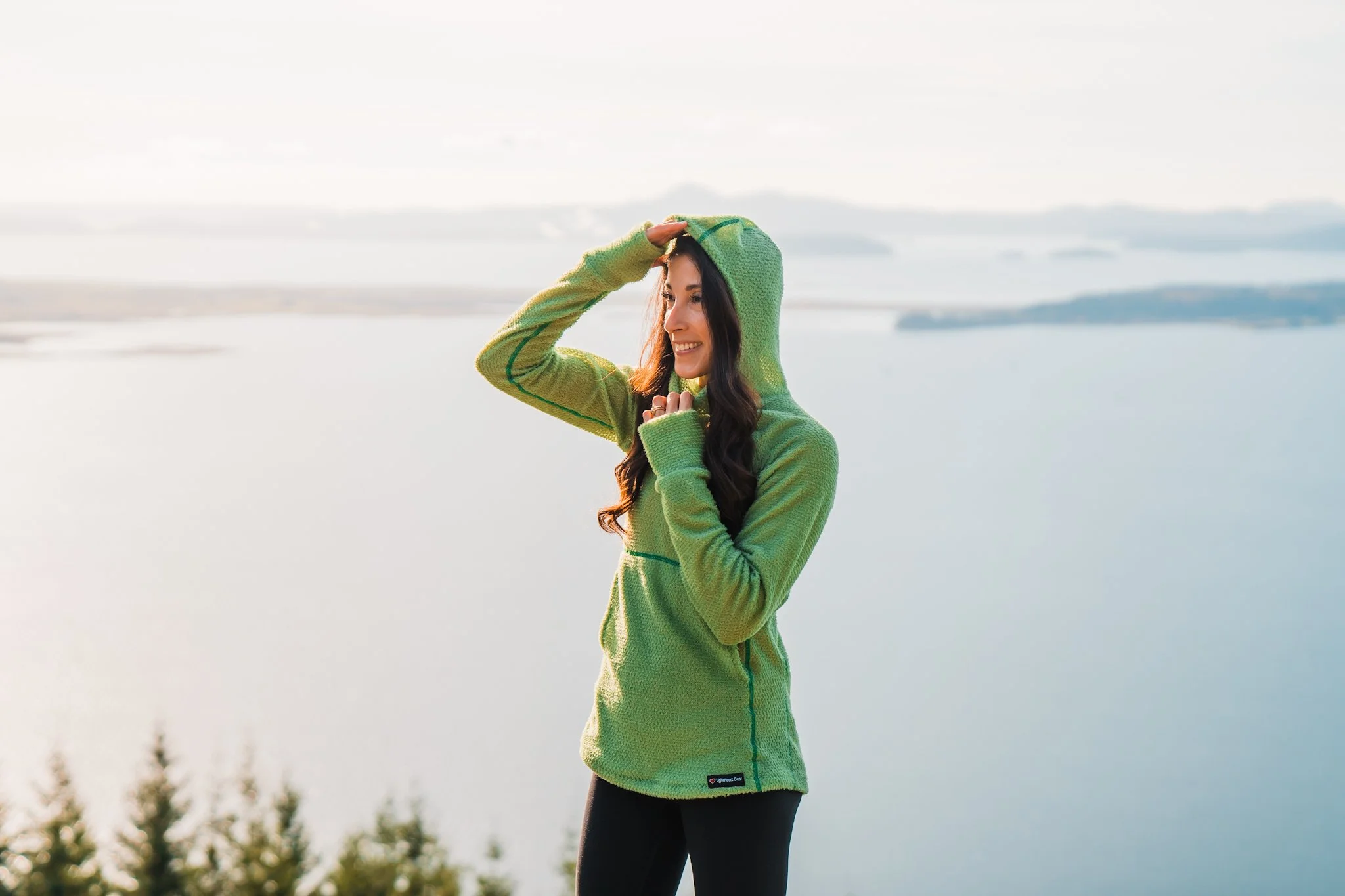 a women in a light green alpha direct fleece hoodie, showing off the hood on a hike