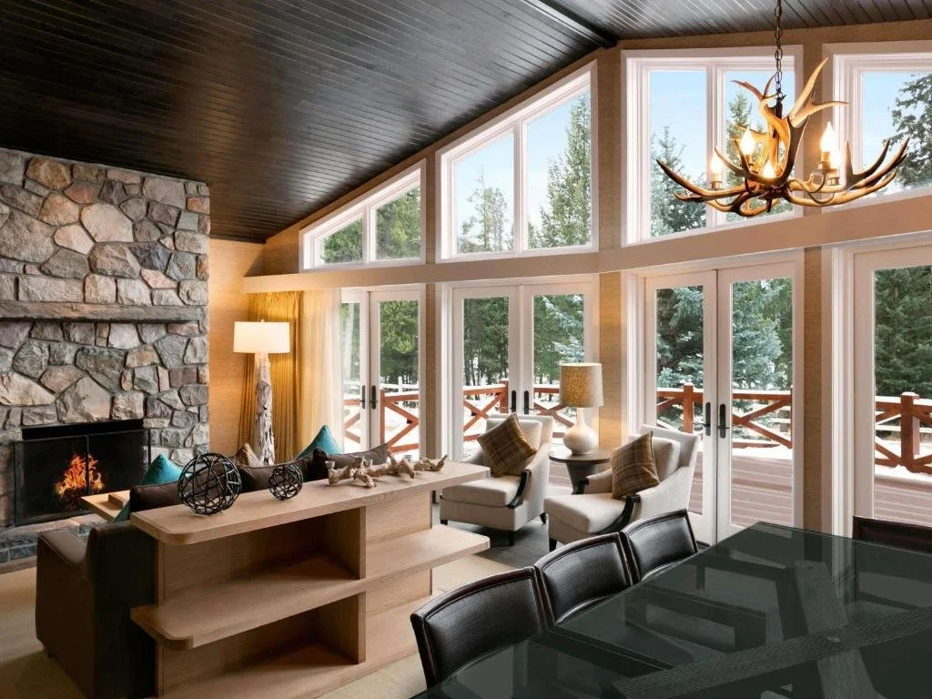 a modern cabin livingr oom with a fireplace and chairs, and windows looking out into nature