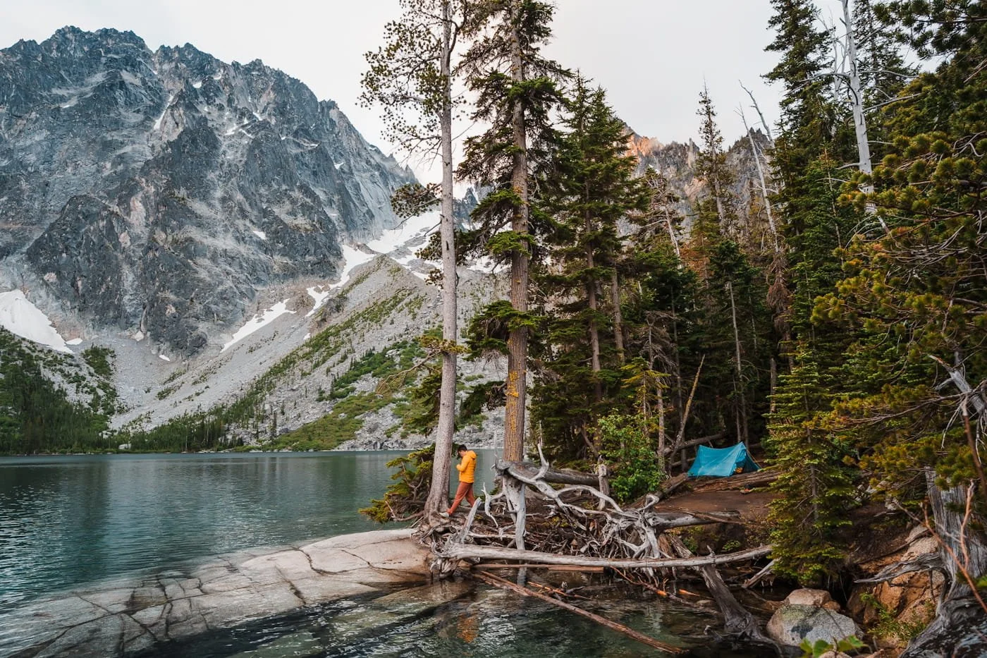 a lakeside campsite at colchuck lake with a man standing and attaching a bear hang with the tent to the side