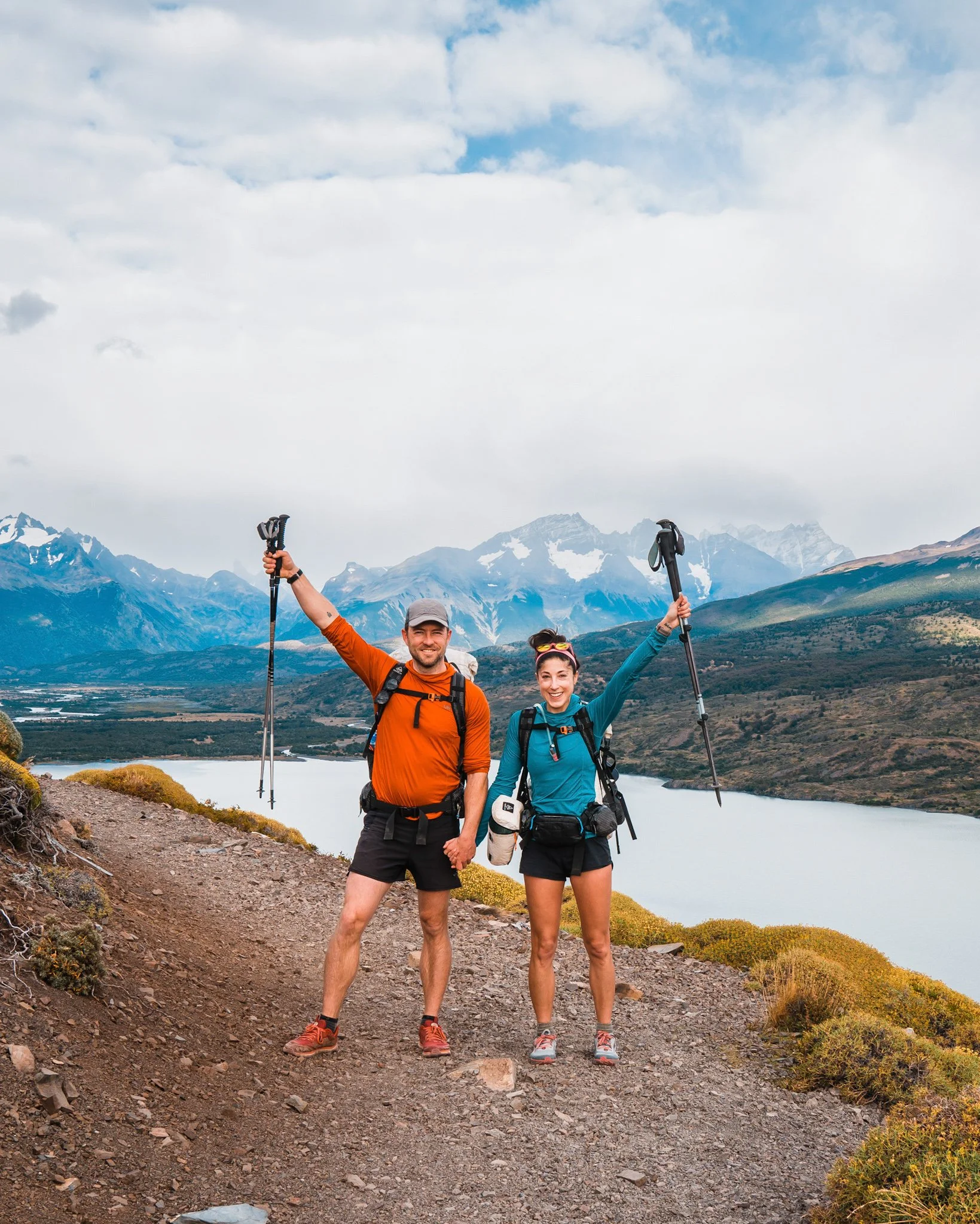 a couple of backpackers on trail, standing with their arms and trekking poles raised, wearing bright colors on the back section of the o-circuit in patagonia