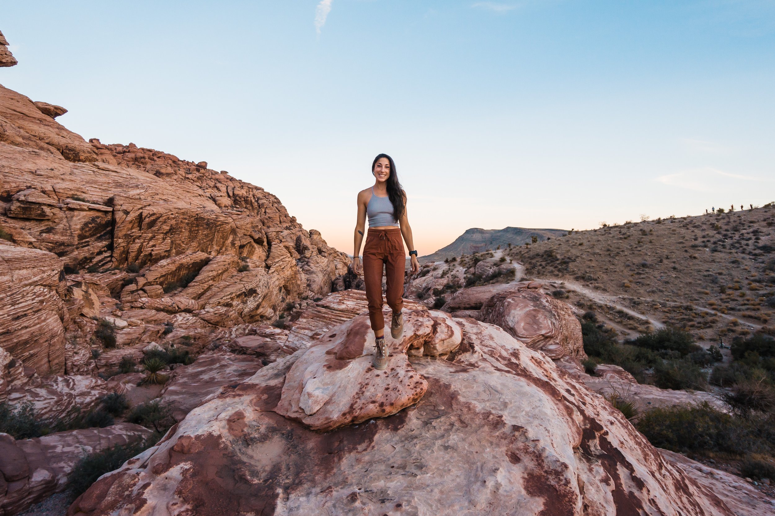 A woman hiking on a rocky desert landscape with red and pink sandstone formations during sunset.