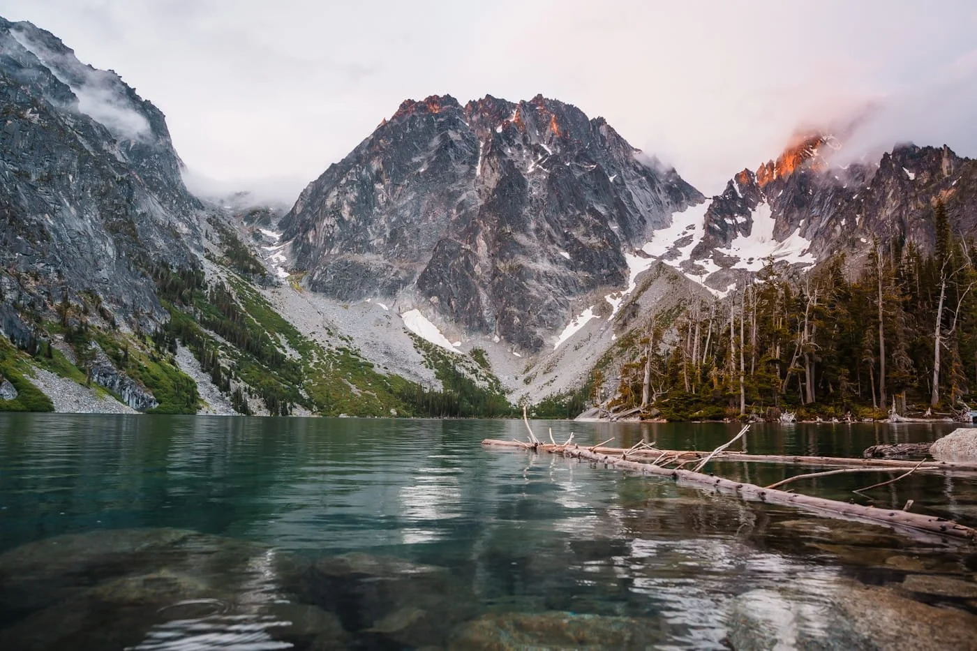 colchuck lake at sunrise with a little rain on the water and fog on the peaks