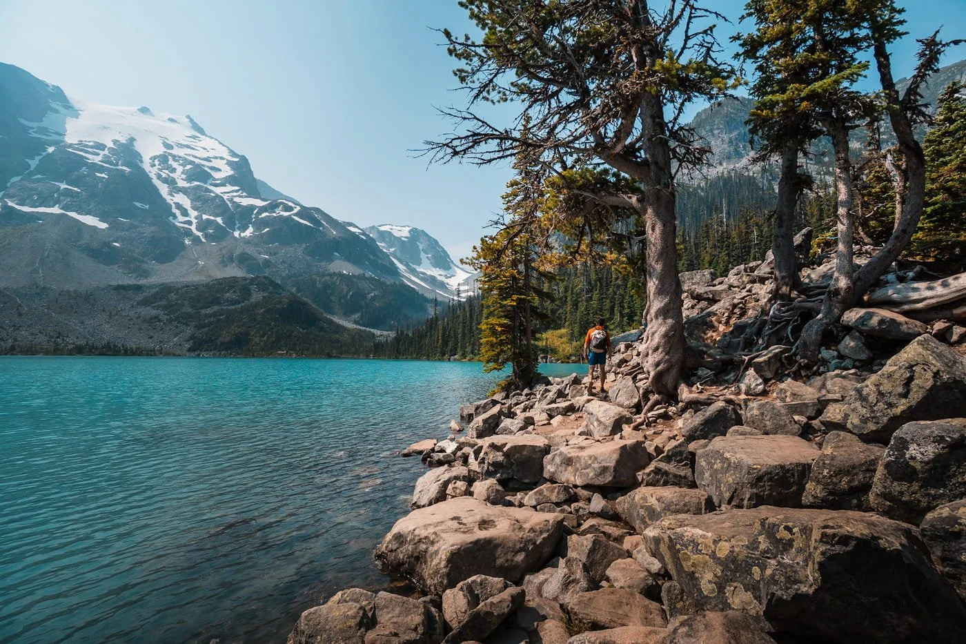 a hiker heading around upper joffre lake across boulders with the lake and mountains to the left