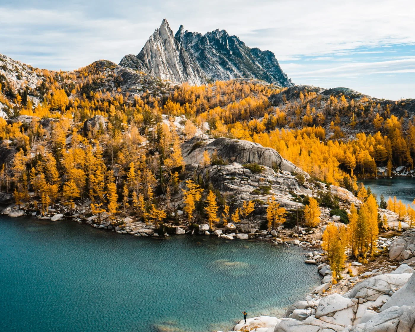 Looking down at a bright blue lake with a tiny person on the lake shore and golden larches and mountains surrounding