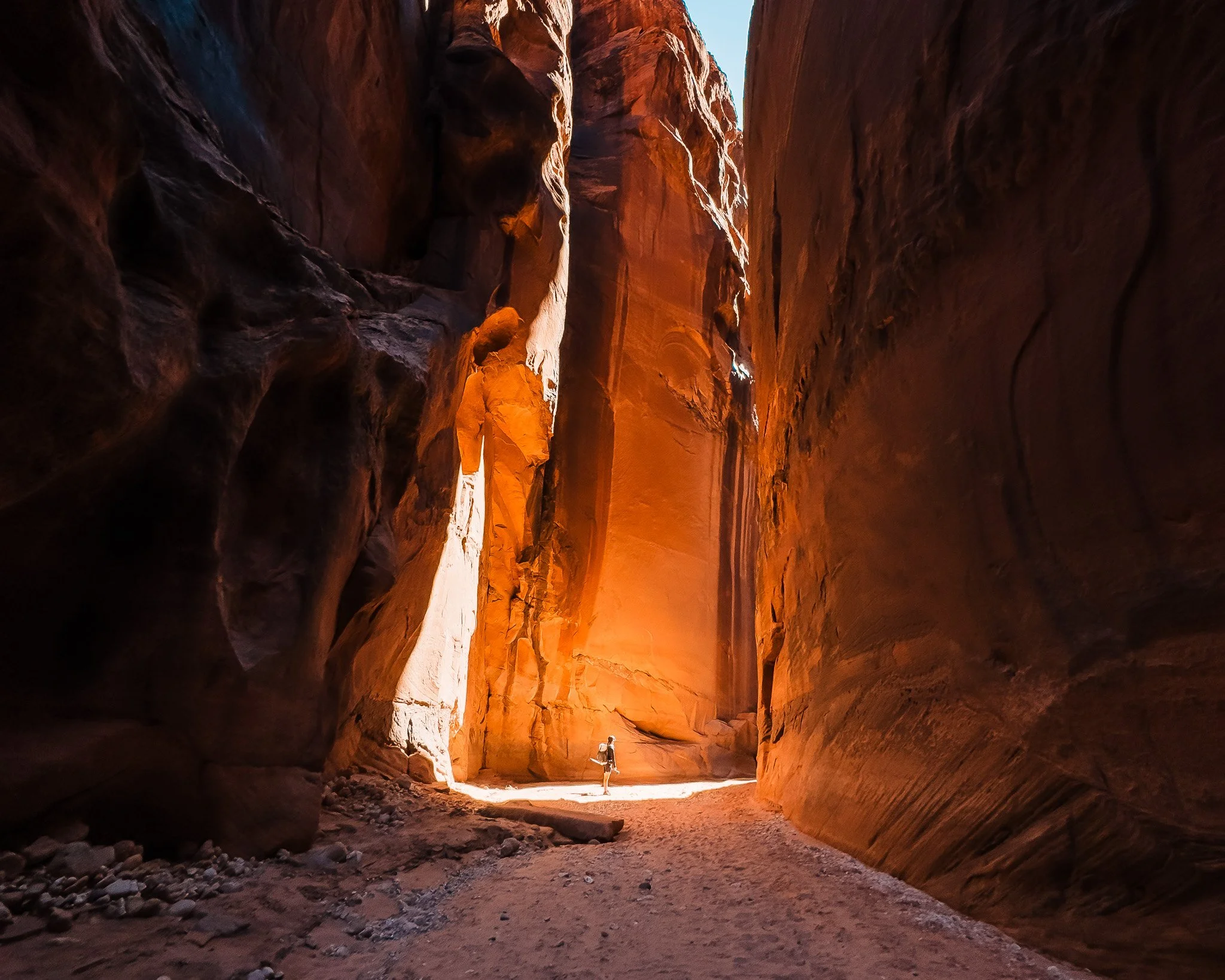 a tiny hiker standing in a sun ray, deep in a slot canyon with tall red rock walls