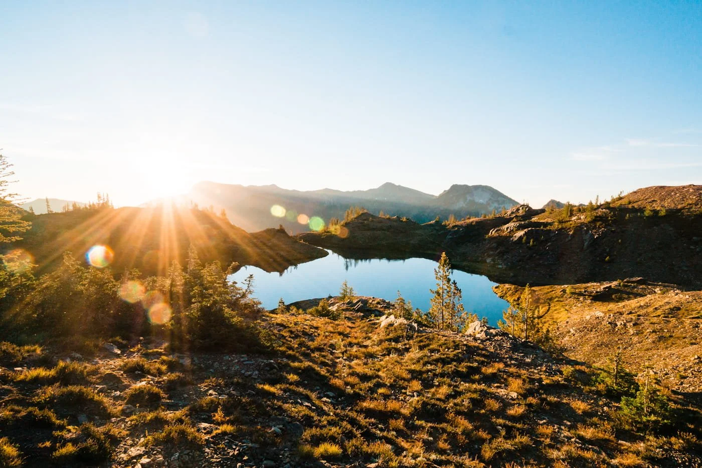 a reflective, blue lake at sunrise with a sun star of light and mountains in the background