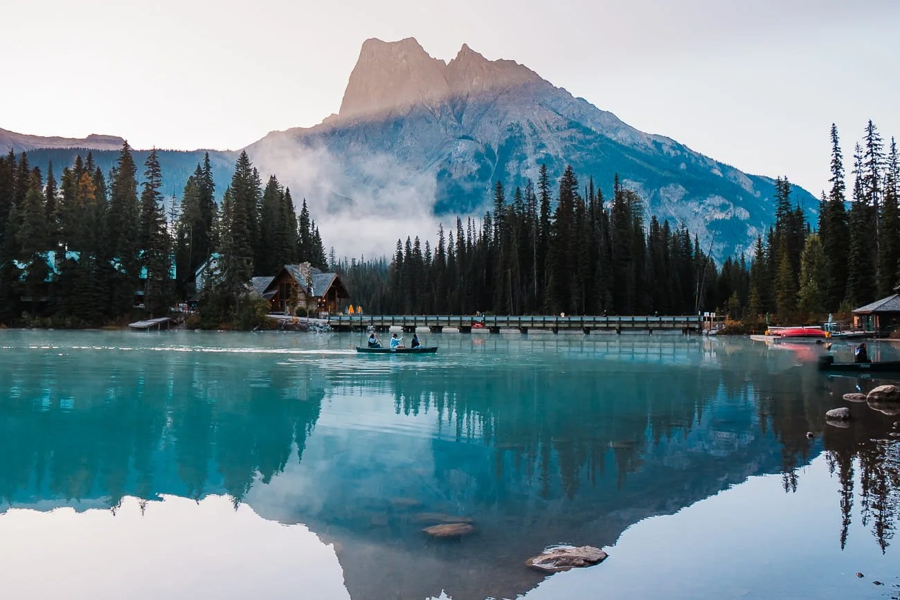 Three people in a canoe crossing Emerald Lake during sunrise
