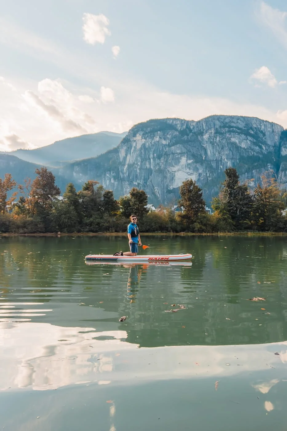 man on a stand-up paddleboard on the Squamish inlet with Stawamus Chief in the background