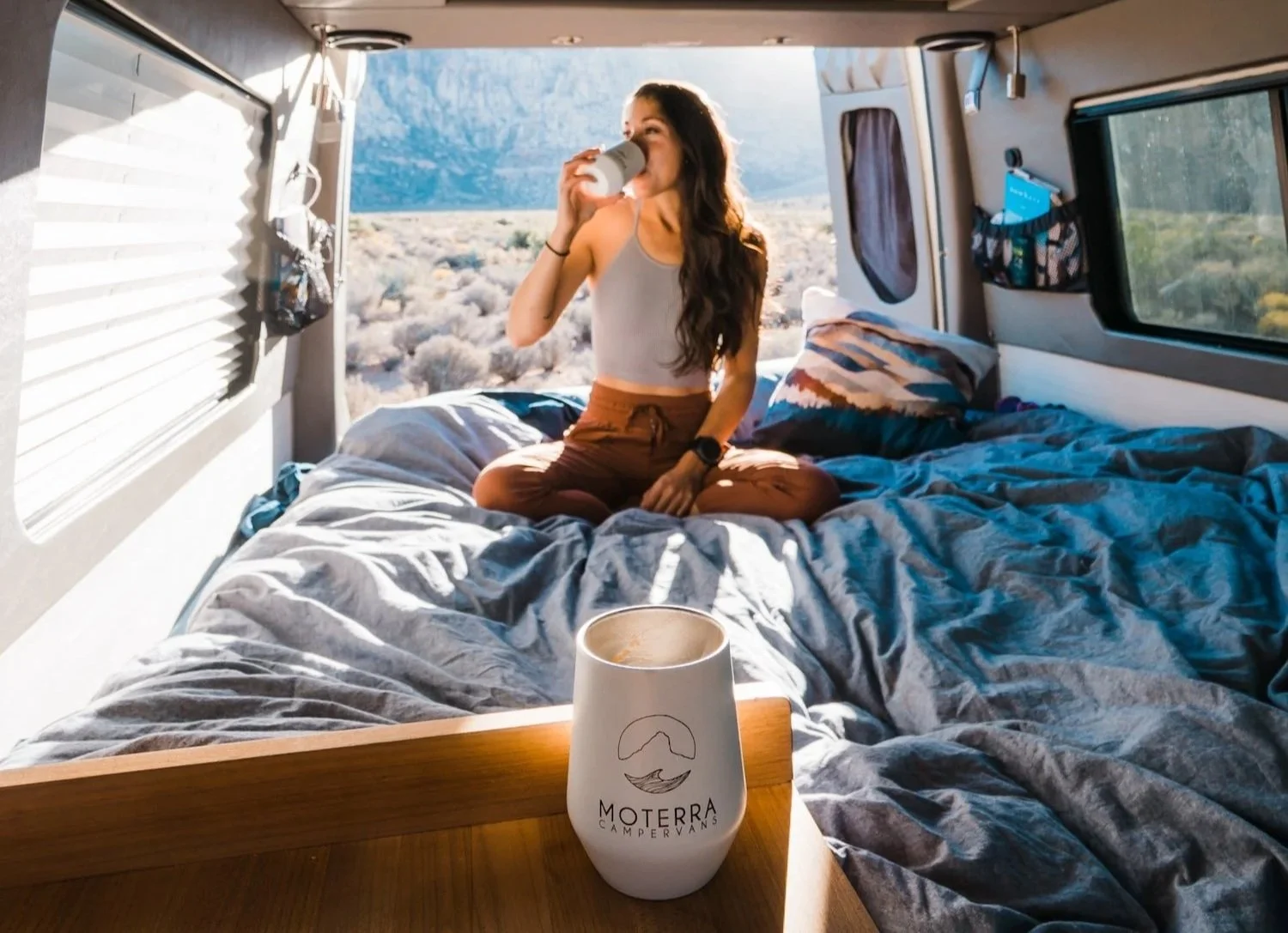 a women sitting on the bed in a campervan, drinking coffee