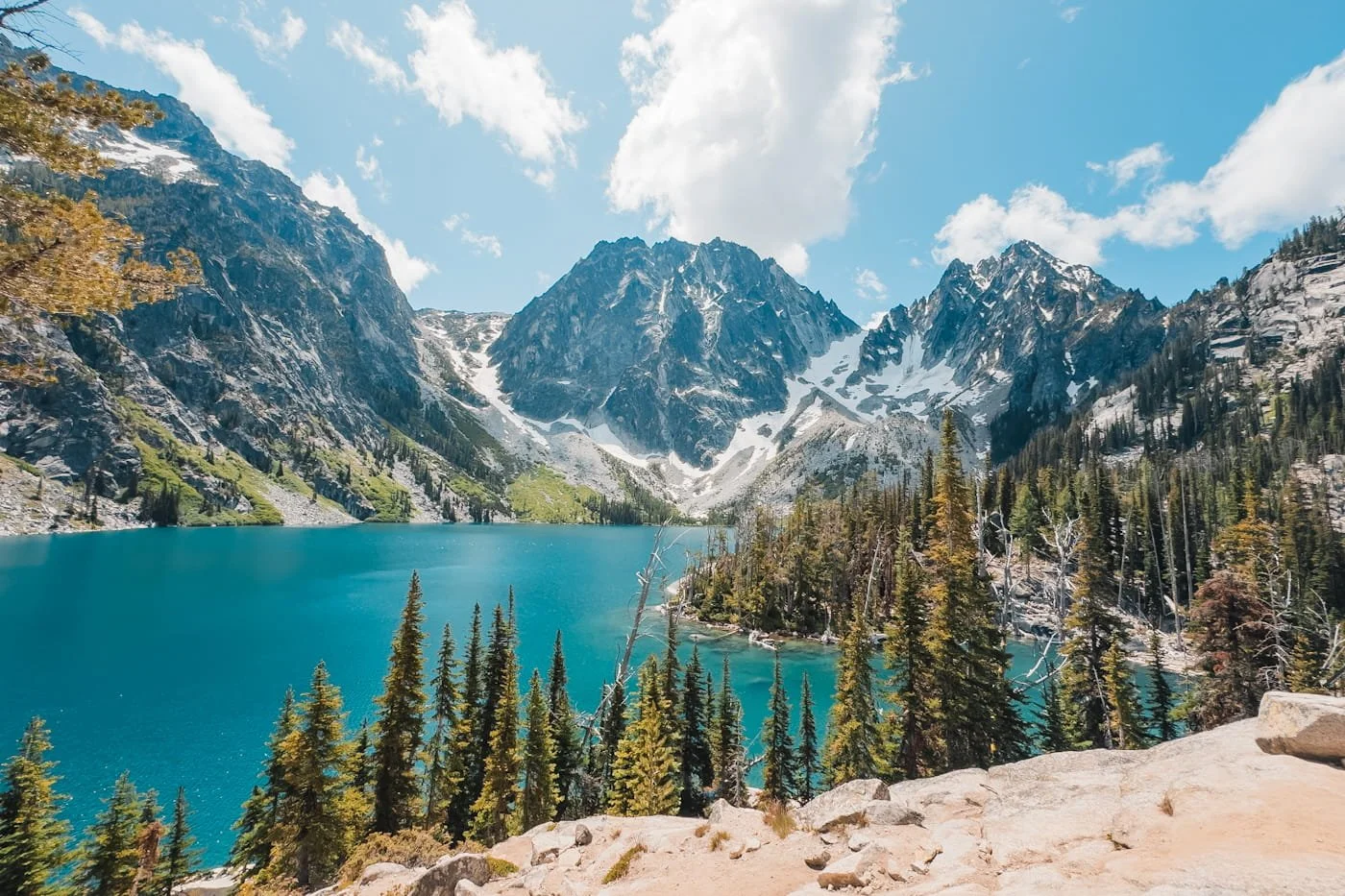 looking out at colchuck lake, a bright blue lake with rocky peaks in the background and alpine trees