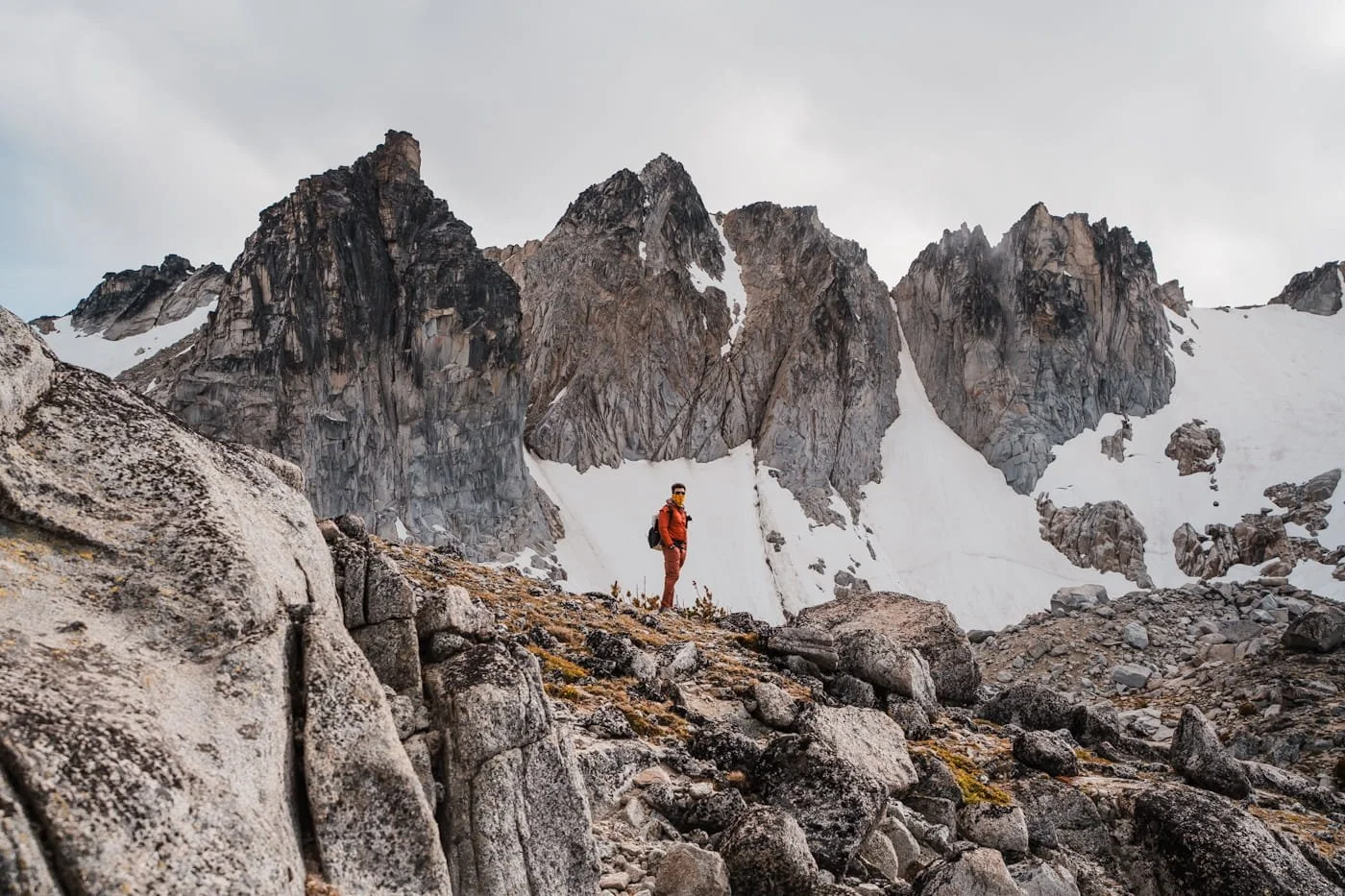 a hiker in red at the top of aasgard pass in the enchantments with rocky peans and snow in the background