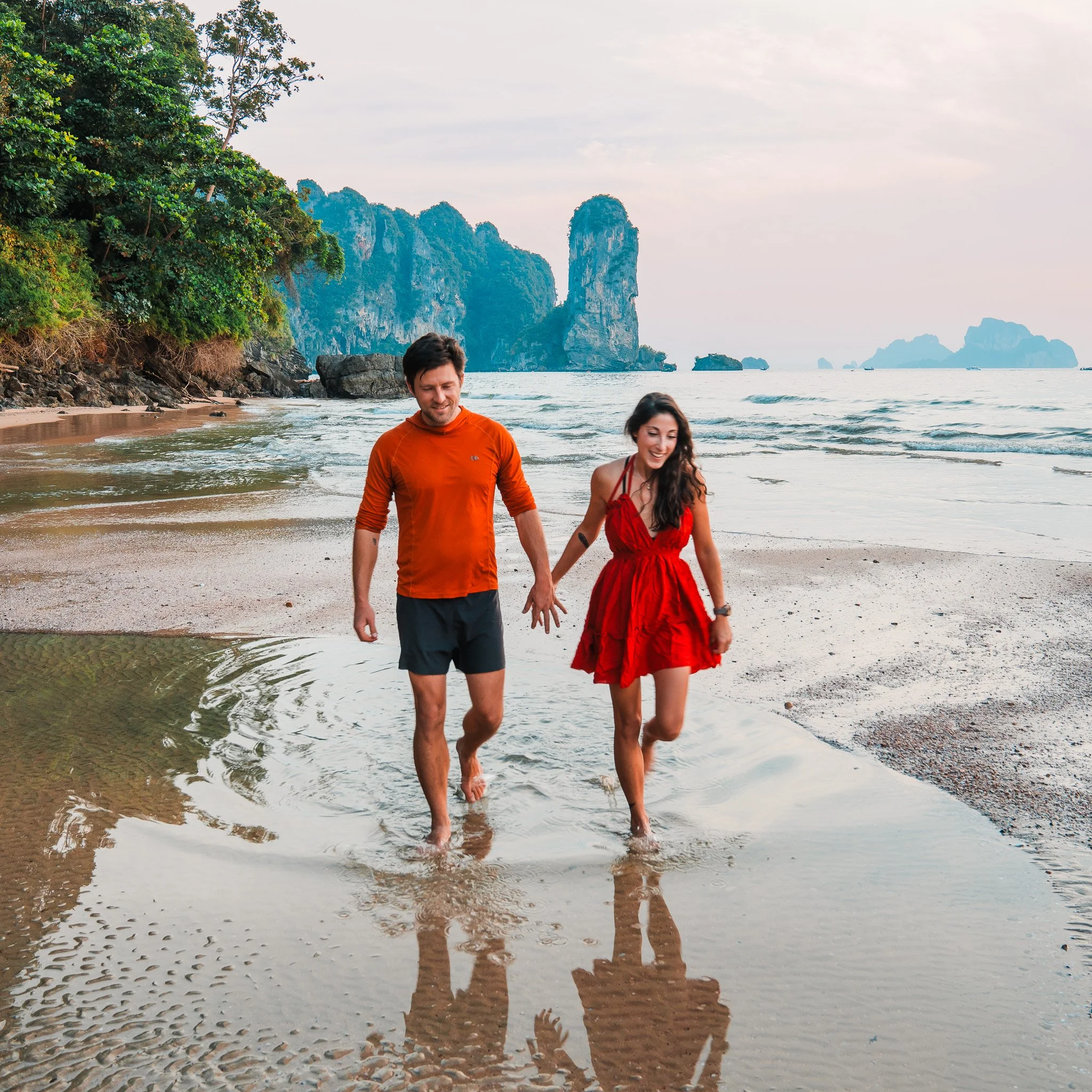a couple wearing red, walking on a beach at sunset in thailand