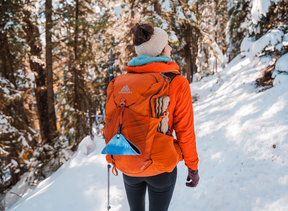 A woman hiking on a snowy trail, wearing a red jacket and orange backpack