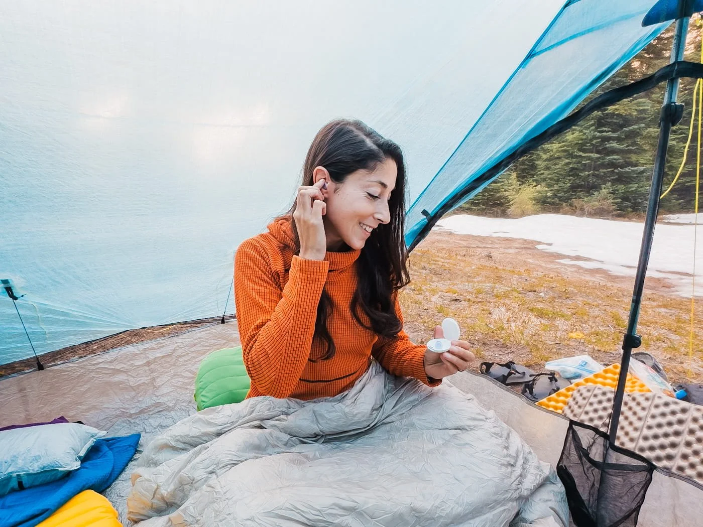 a woman in a tent while backpacking, putting ear plugs in her ears