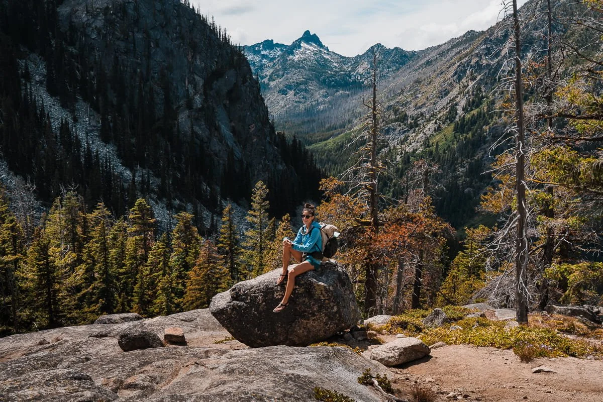 A hiker sitting on a rock with mountain views in the background