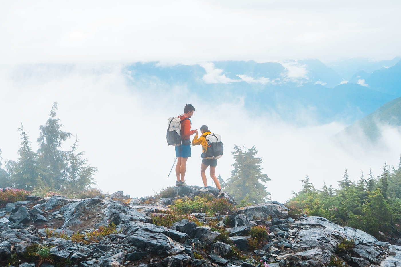 A couple backpacking with white and black hyperlite packs, on a rock overlooking a foggy view
