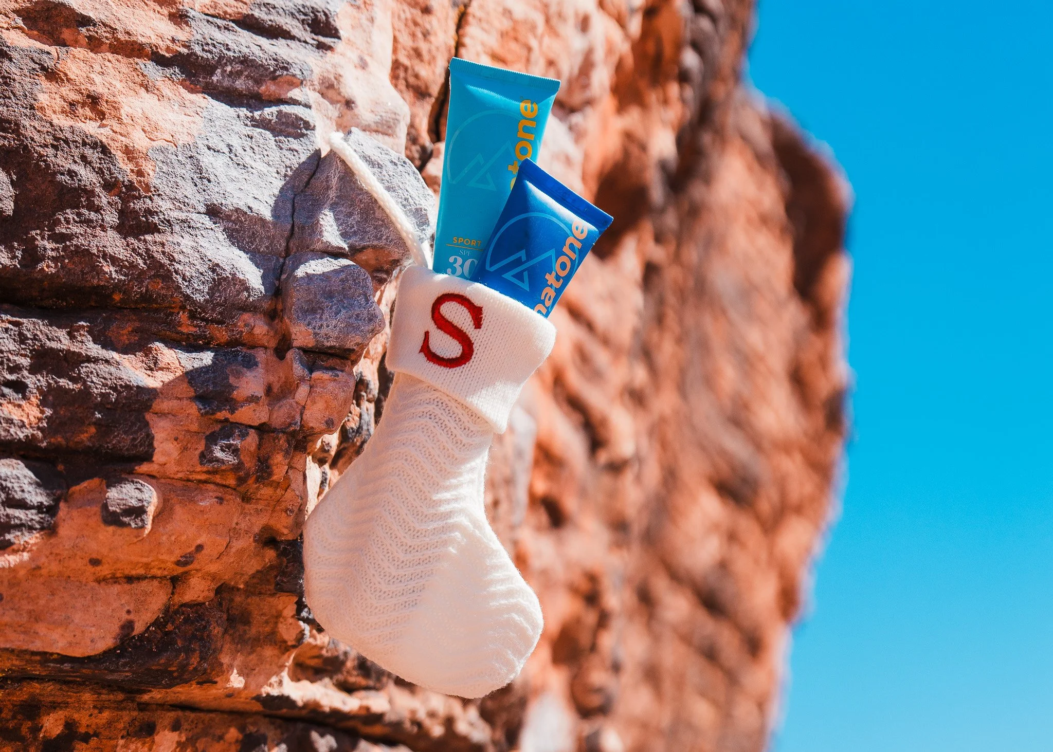 a small white stocking with an S on it, with two tubes of sunscreen sticking out, hanging on a rock wall in the desert