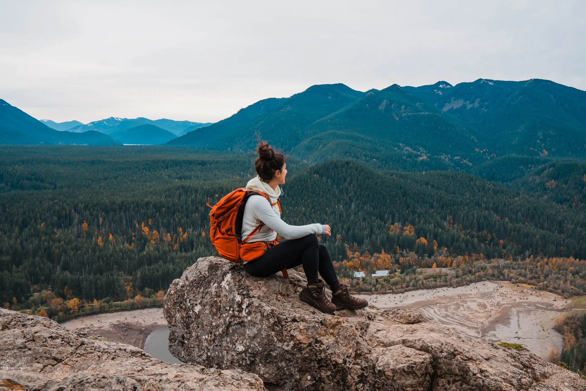 a women sitting on a rock outcropping looking out at the mountains, wearing hiking gear and a day pack