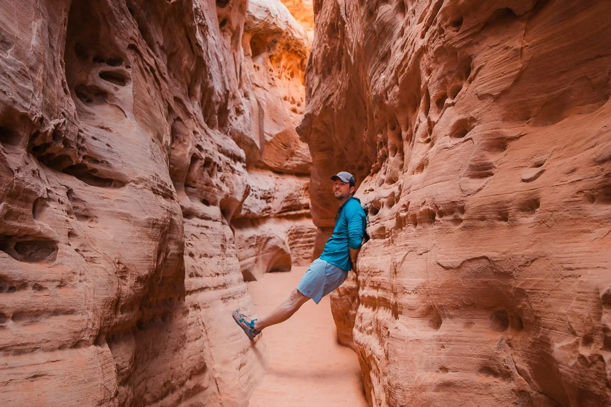 a hiker balancing on the walls in a sandy slot canyon