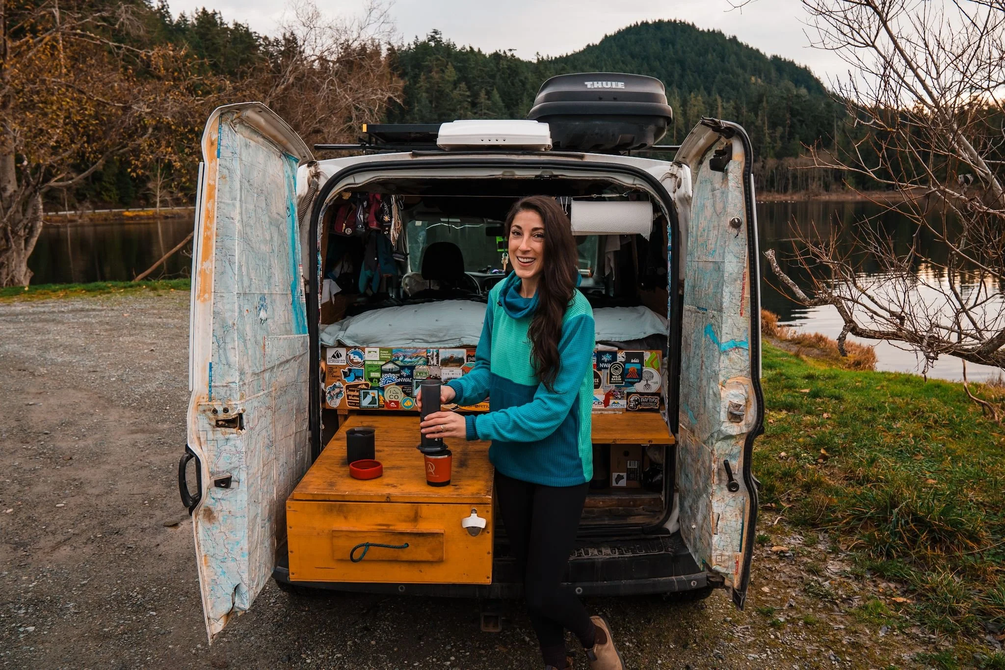 a woman wearing a multicolor fleece hoodie, making coffee at the back of her small campervan