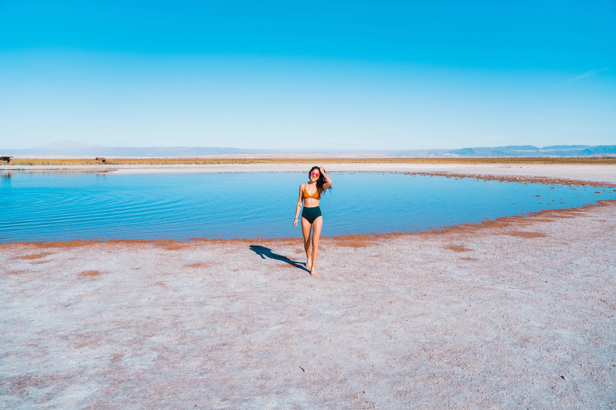 a women walking towards the camera in front of a salt pool in the atacama desert