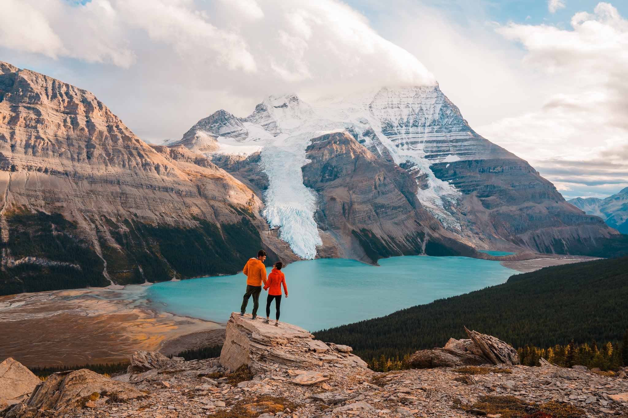 A couple standing on a rock above Berg Lake and Mount Robson in the background