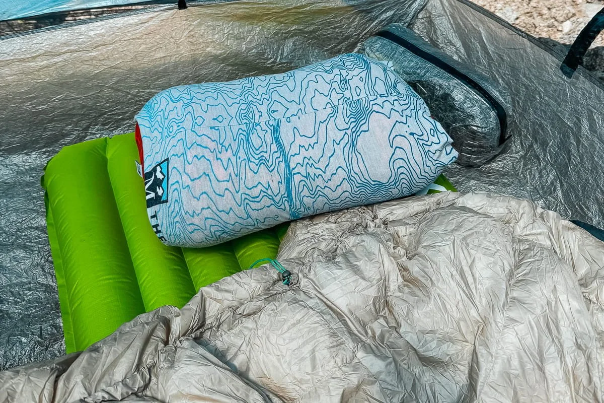 A green sleeping pad with grey quilt and pillow inside of a tent while backpacking