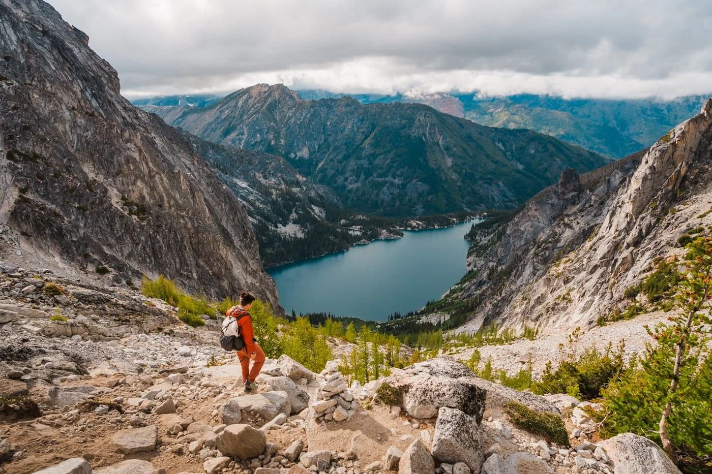 a hiker on their way down Aasgard pass in the enchantments with a blue colchuck lake below