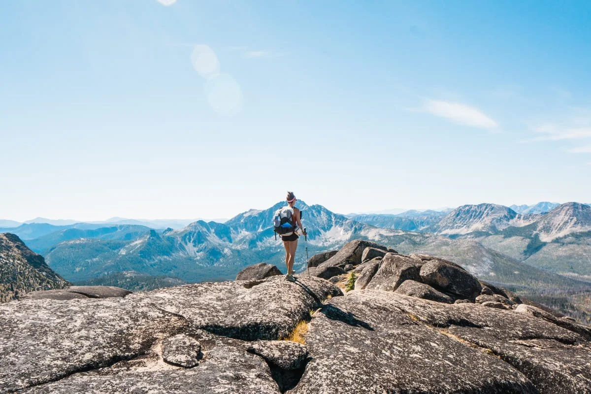 a hiker walking on a rock slab on top of a peak in the pasayten wilderness