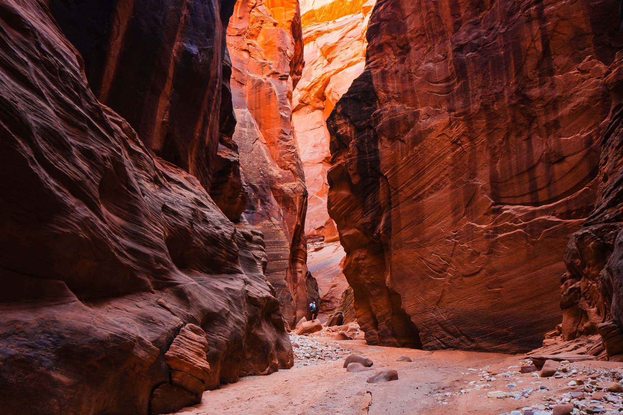 big, red canyon walls with a tiny hiker standing on a rock deep in the canyon