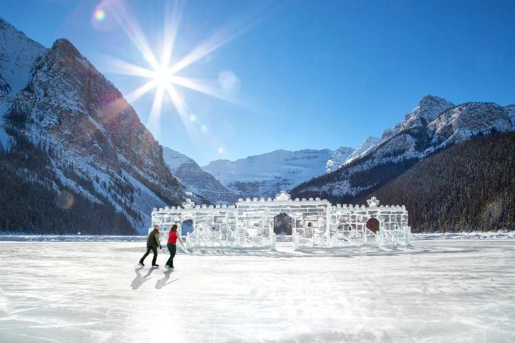 a couple ice scating on Lake Louise with an ice castle and mountains in the background