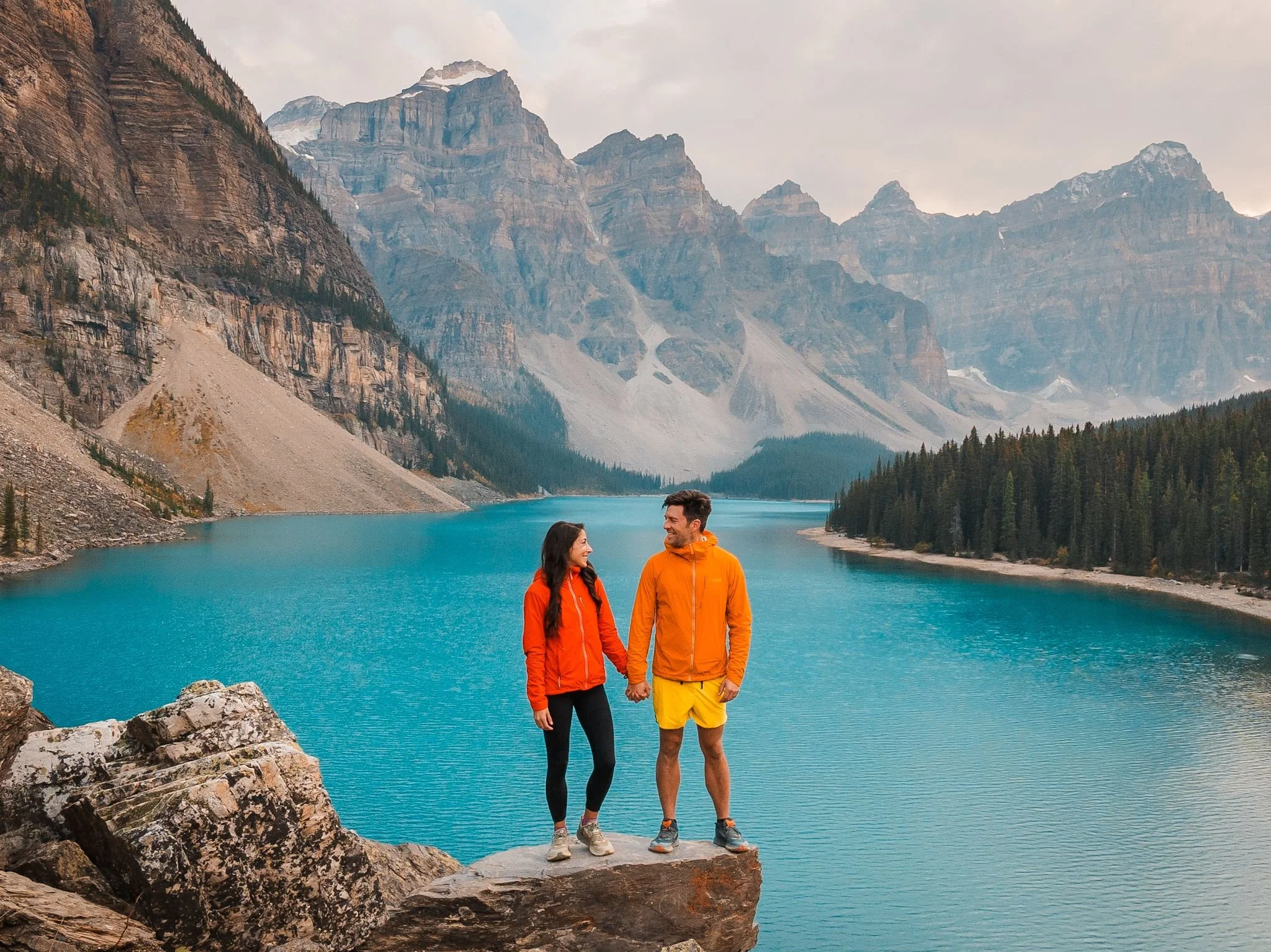 a couple standing in front of moraine lake in banff wearing bright colors