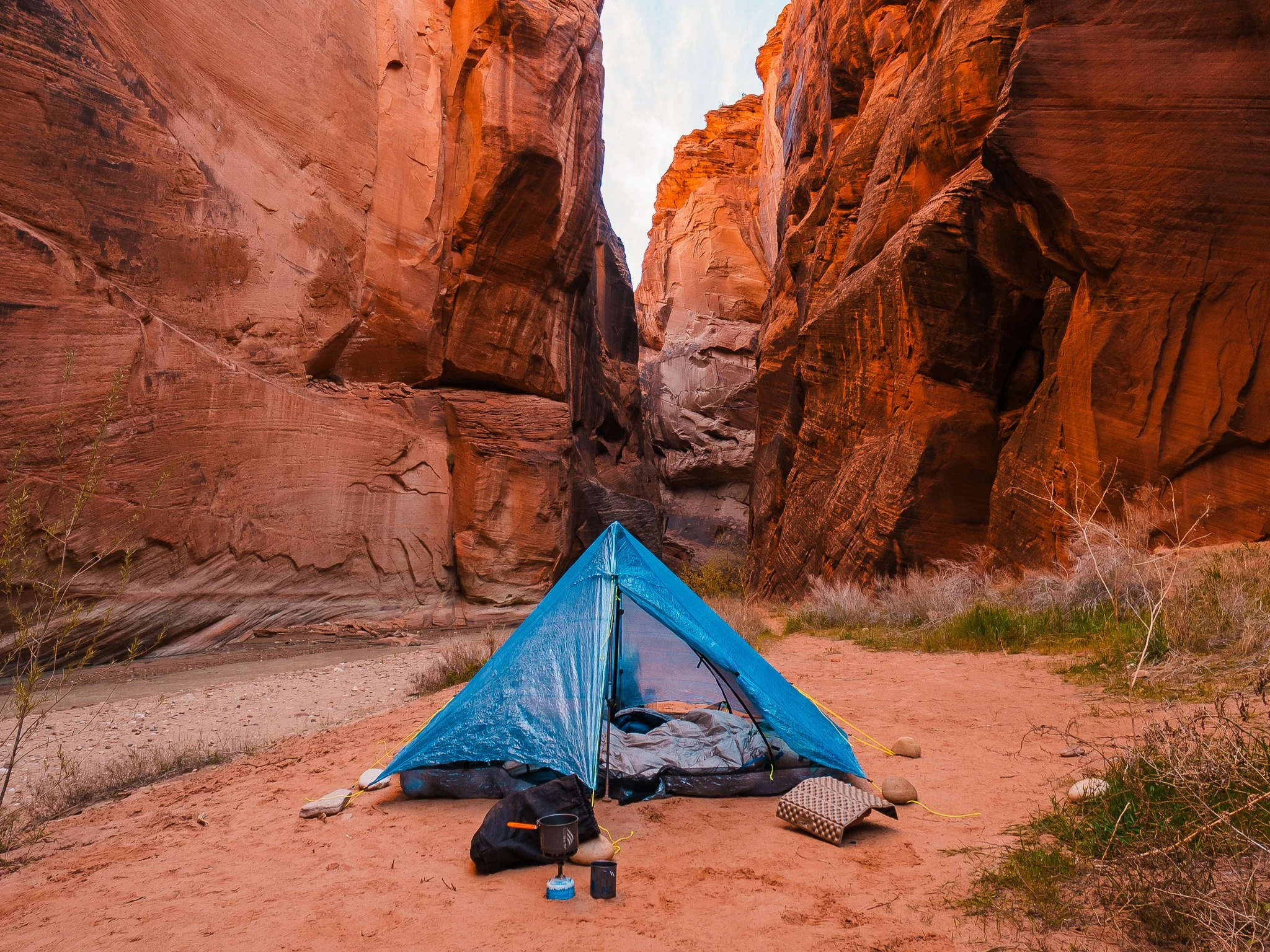 a blue tent pitched on a sand bar with high canyon walls on all sides