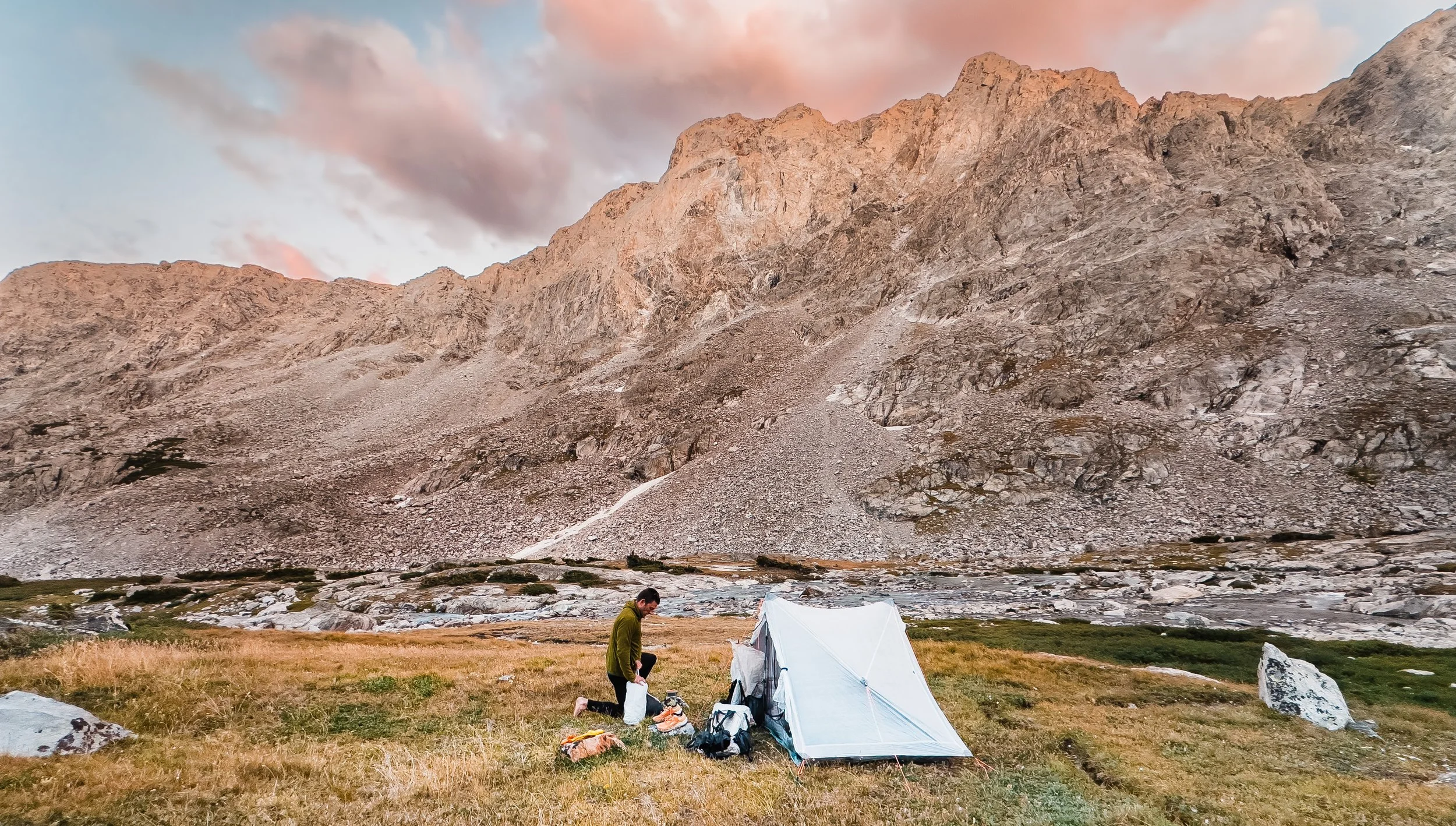 Backpacker packing tent in basin below Gannett Peak on Wind River High Route