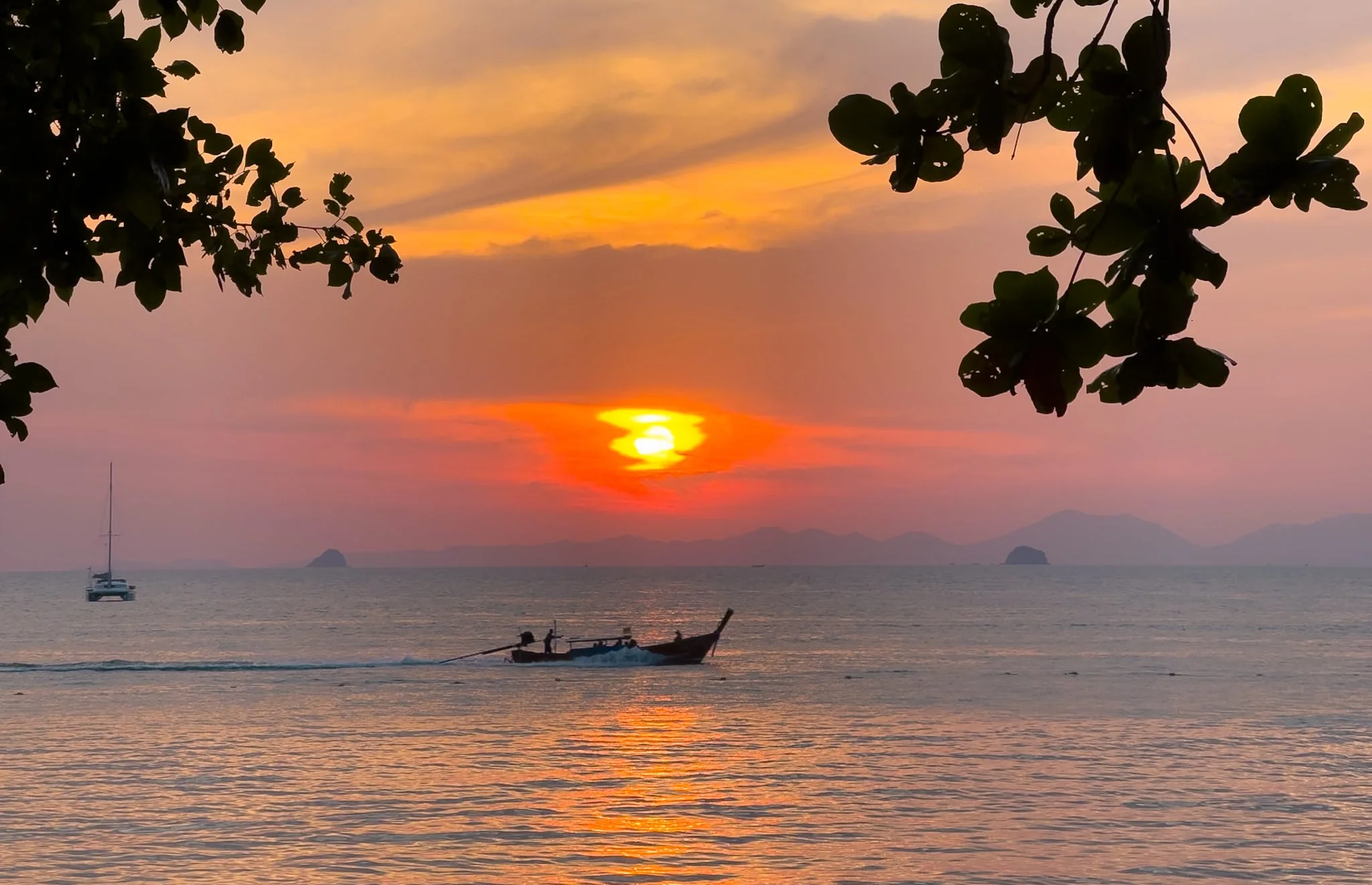 a pink and orange sunset looking out at the water with a traditional long tail boat passing through