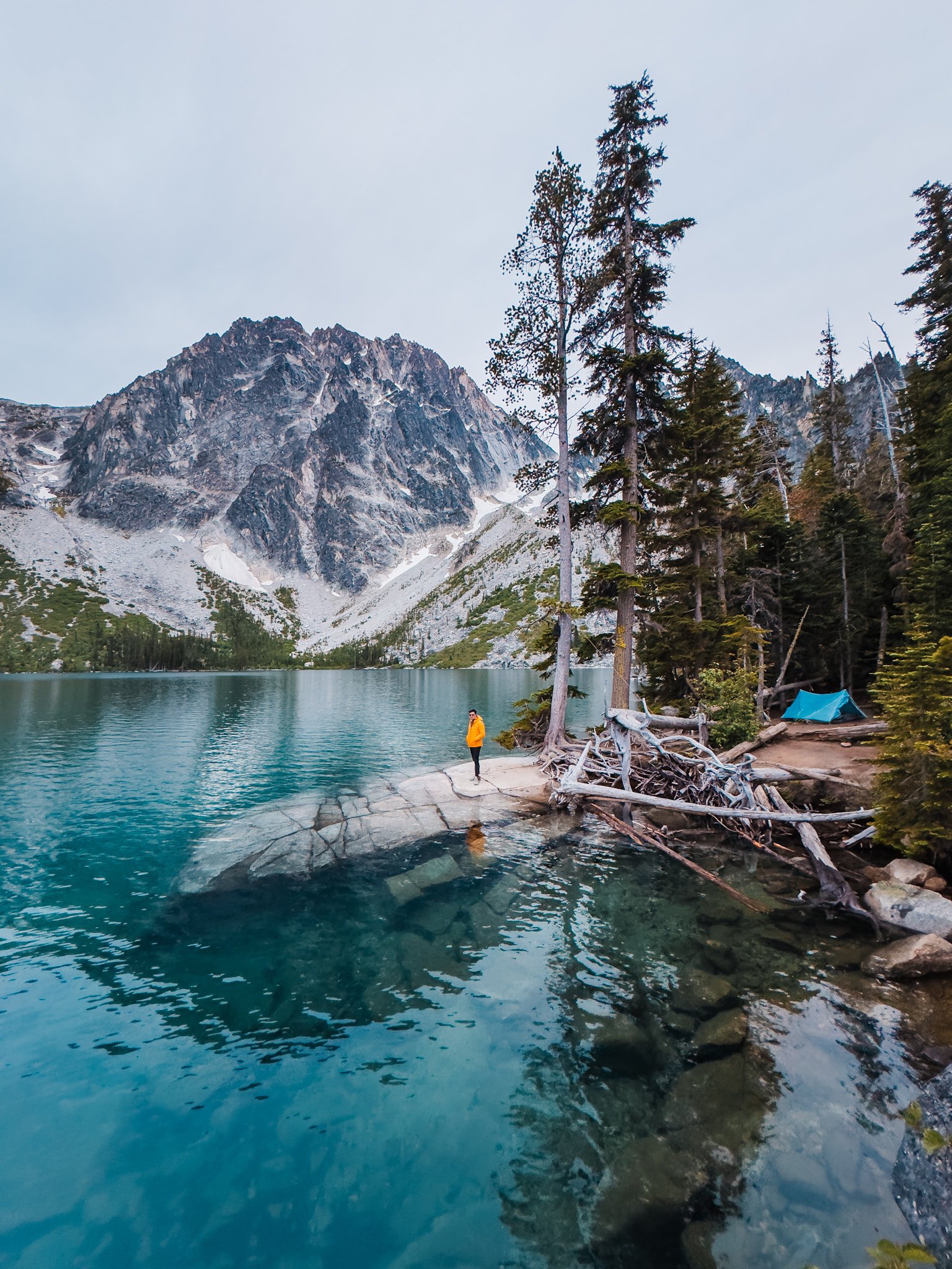 A camper standing on a rock next to their lakeside campsite at colchuck lake in the enchantments