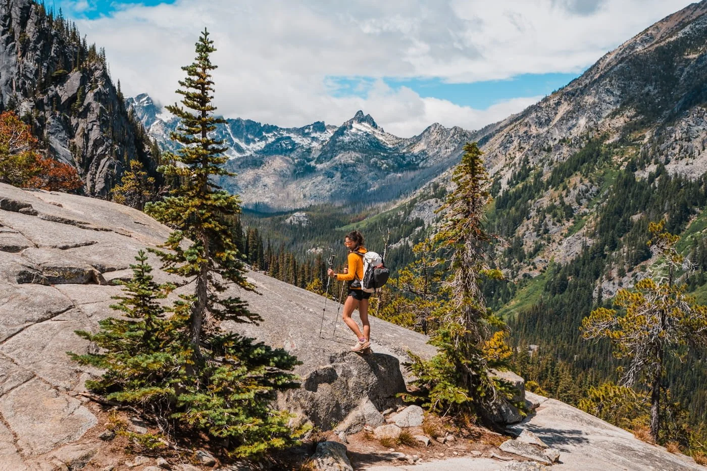 a woman with a backpacking pack on standing on a rock with mountains in the background, in the enchantments