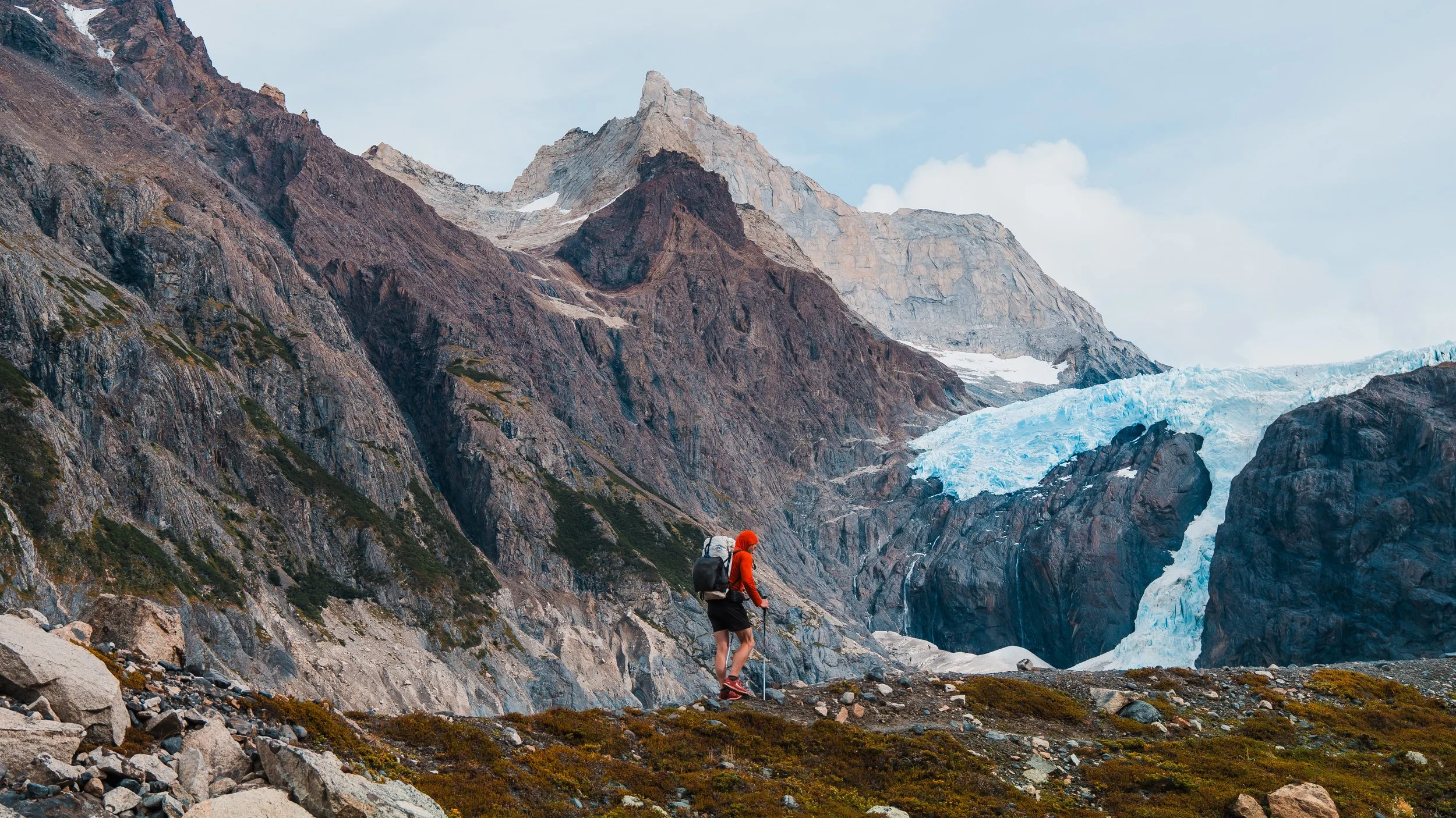 man backpacking along a ridge line in patagonia with a glacier and craggy mountains in the background