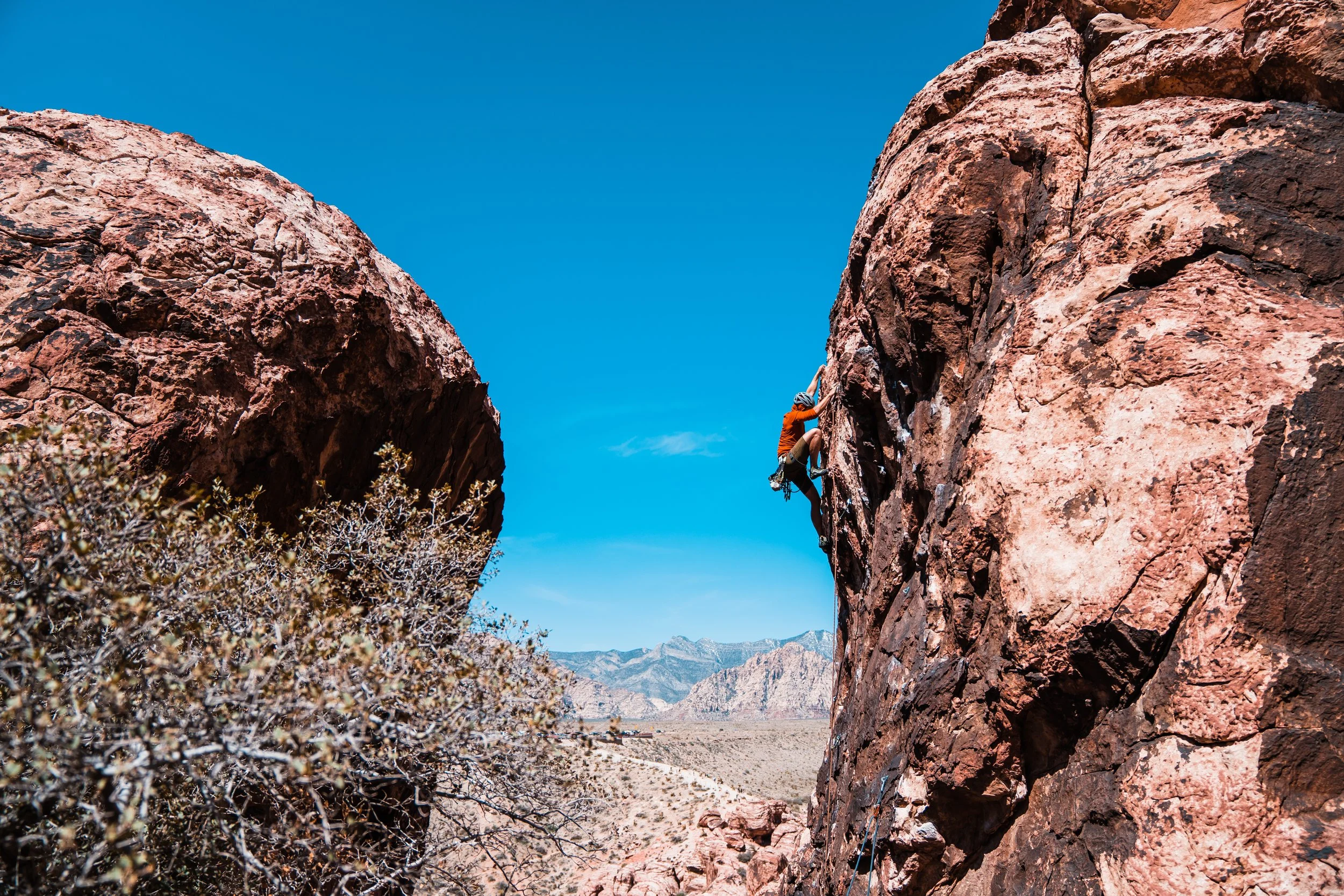 A person climbing an outdoor rock face in a desert landscape with clear blue sky.