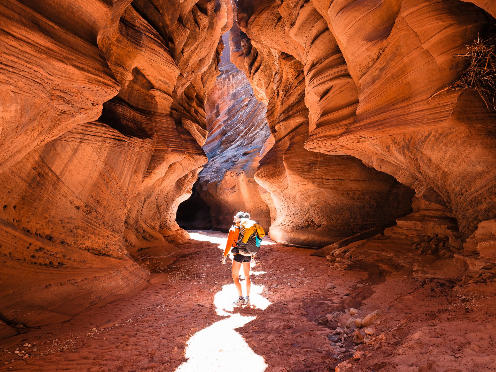 a women wearing a backpacking pack, deep in a sandstone slot canyon with wavy orange walls and light streaming through