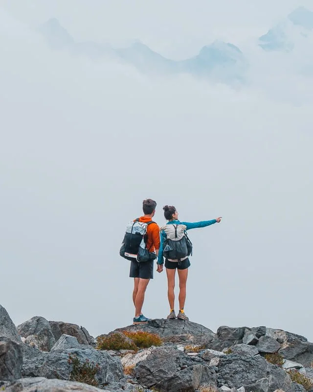 a couple of backpackers standing on rocks, with fog and clouds in the background
