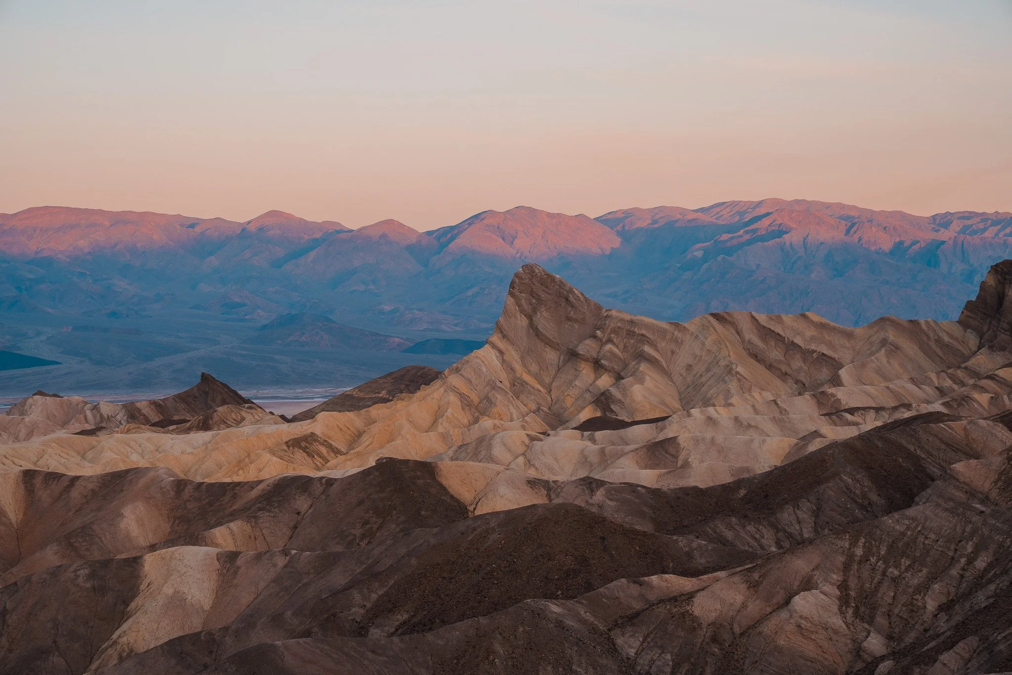 a pink and orange sunrise over stripped sand dunes in death valley